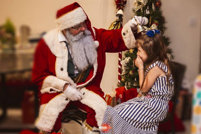 Papai Noel em visita de família, conversando com pai e filho perto da lareira